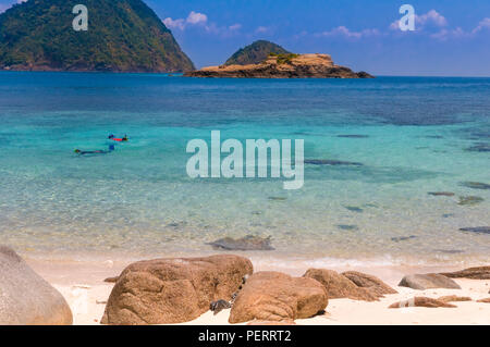 Lovely scene of two tourists snorkeling in the in the shallow clear turquoise waters of Rawa beach, an island near Perhentian Kecil in Malaysia with... Stock Photo