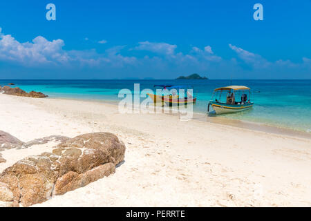 Three tourist boats anchoring on a white powdery sandy beach, a blue sky and a small island on the horizon makes it a gorgeous scene of the... Stock Photo