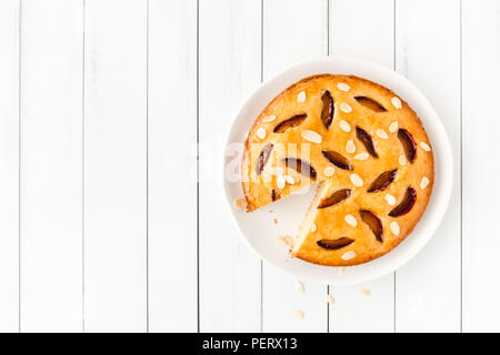 Cut homemade plum cake on porcelain cake plate and white wood planks. Stock Photo