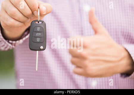 Close up of unrecognizable man in shirt holding car keys and showing thumbs up. Stock Photo