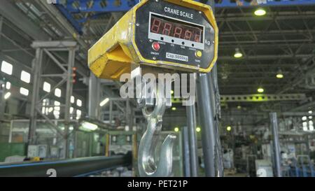 RUSSIA, ANGARSK - JUNE 8, 2018: Industrial type 5000 kg digital weight scale hanging on hook of crane, with clipping path. Manufacture of plastic water pipes factory. Stock Photo