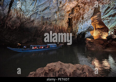 A tourist boat navigates on a natural lake inside Phong Nha Cave with column rock formations in the background. In Phong Nha National Park, North-Cent Stock Photo