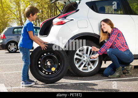 Portrait of little boy rolling donut tire while his mother unscrewing wheel nuts, trying to change flat tyre Stock Photo