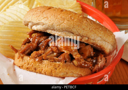 A pulled pork sandwich on a bun with potato chips in a basket Stock Photo