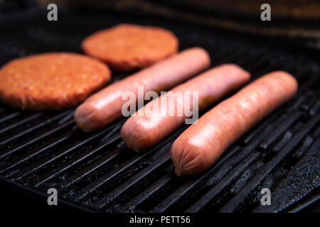 Fresh uncooked barbecue sausages, burgers and bread ready to be grilled, sitting on a grill Stock Photo