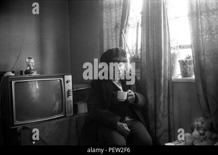 East End London 1970s, poverty in Britain, an elderly black British woman in her council estate flat on the Stonebridge Estate.  Isolated and living alone in a single room plus small kitchen and bathroom. All in very bad condition, the flat is damp and very cold, she is dressed in her hat and coat and drinks a cup of tea to keep warm. Haggerston, East London, England 1978. 70s UK HOMER SYKES Stock Photo