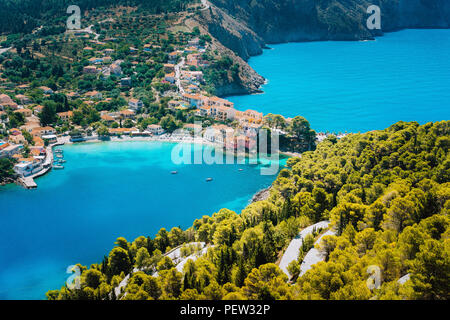Panoramic view to Assos village Kefalonia. Greece. White lonely yacht in beautiful turquoise colored bay lagoon water surrounded by pine and cypress trees along the coastline Stock Photo