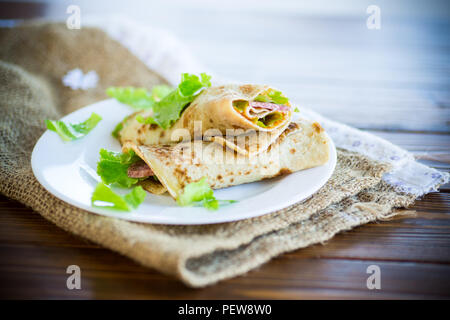 thin pancakes with salad leaves and bacon in a plate on a wooden table Stock Photo
