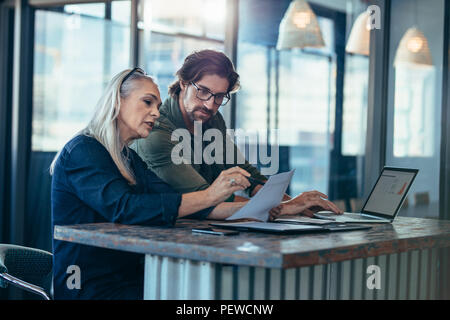 Senior woman discussing work with male colleague. Two business associates working together in office and talking over a business report. Stock Photo