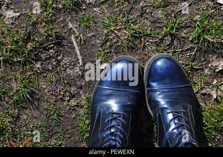 blue boots standing on dirty ground in a forest while fresh grass starts to grow Stock Photo