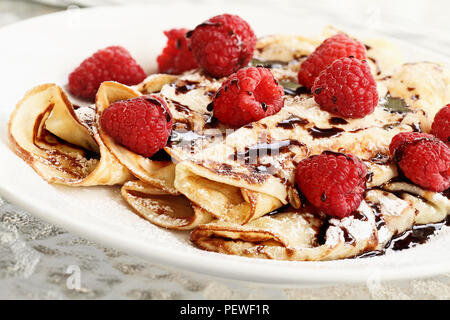 Delicious golden palacinky pancakes or Czech Pancakes with fresh raspberries and sweet chocolate syrup. Extreme shallow depth of field. Stock Photo