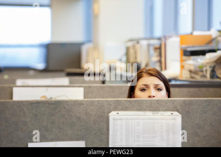 A young Caucasian woman looking concerned over the top of her cubicle in a corporate office. Stock Photo