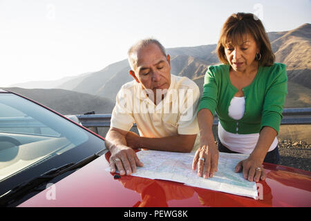 An Hispanic senior couple checking a paper map while pulled over at rest stop on a road trip. Stock Photo