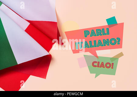 some flags of Italy and the question parli italiano? do you speak Italian? written in Italian, on a pink background Stock Photo