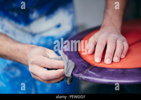Man sanding and shaping a surfboard in a workshop Stock Photo