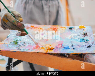 Wooden art palette with oil paints. Mixing colors together. Artistic instrument with many colors. Working tool with squeezed out tubes of paint. Stock Photo