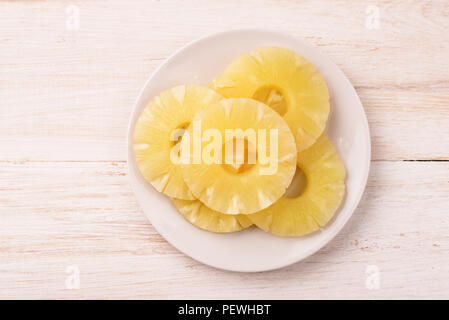 Top view of canned pineapple slices on plate on wooden background Stock Photo