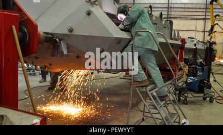 A journeyman welder removes a panel from a Light Armored Vehicle (LAV) using a plasma cutter at Production Plant Barstow, Yermo Annex, Marine Corps Logistics Base Barstow. The LAV is secured on a trunnion, a device that supports it at both ends and allows full rotation for complete access during repairs. This setup enables welders to reach all angles, edges, and curves efficiently, maintaining vehicles damaged in the field. The process ensures operational readiness of Marine Corps armored vehicles. Stock Photo