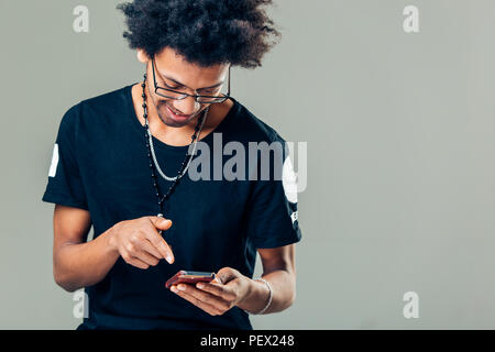 Serious young black male in trendy rectangular glasses looking through pcitures via social media, using cell phone Stock Photo