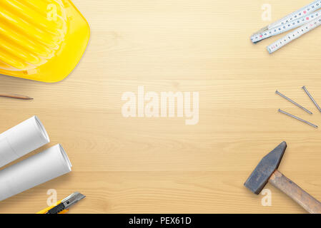 Helmet, tools and plans on wooden work desk. Copy space in the middle. Flat lay. Top view. Stock Photo