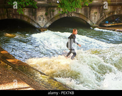 MUNICH, GERMANY - JULY 24, 2018 -  Munich, surfer girl in diving  suit rides the artificial wave on the Eisbach, small river across the Englischer Gar Stock Photo