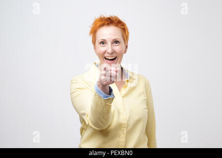Happy mature fashion woman with red hair posing for the camera while pointing at you. She is so happy to see you Stock Photo
