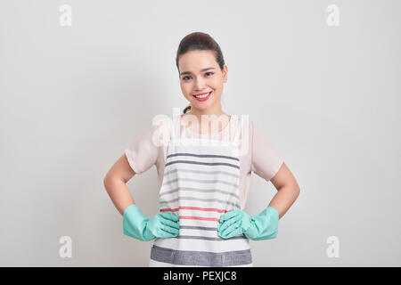 Young attractive smiling housewife in striped apron, blue gloves isolated on white background. Beautiful housekeeper woman standing with arms akimbo l Stock Photo