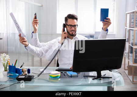 Smiling Young Businessman Doing Multitasking Work At Workplace Stock Photo