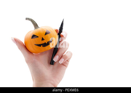 Woman's hand holding small painted halloween pumpkin and black marker pen isolated on white background. Holiday decoration concept. Stock Photo