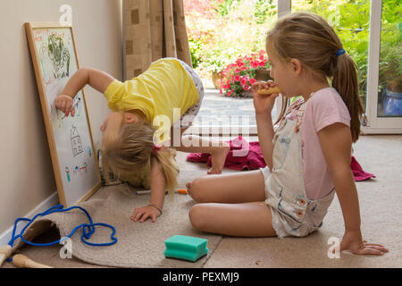 young two year old girl sitting with five year old sister, drawing with coloured pen on white board, being artistic, Stock Photo