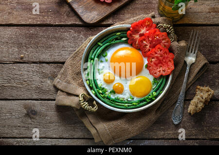 Sunny side fried eggs in a copper pan with tomatoes and green beans, copy space. Stock Photo