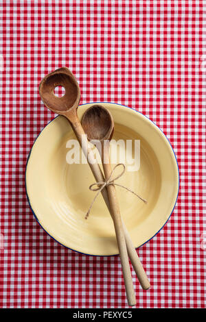 Rustic place setting. Empty plate, wooden kitchen utensils and red tablecloth, top view Stock Photo