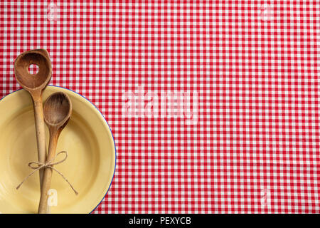 Rustic place setting. Empty plate, wooden kitchen utensils and red tablecloth, top view, copy space Stock Photo