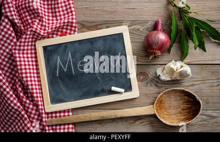 Menu text on a chalkboard, herbs and a ladle on red tablecloth and wooden table, top view Stock Photo