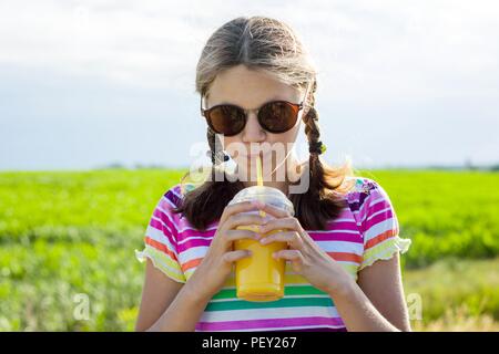 Happy teen girl drinking orange juice at hot summer day. Outdoor Stock Photo