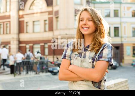 Outdoor portrait of teenager 13, 14 years old, girl with crossed arms, city street background. Stock Photo