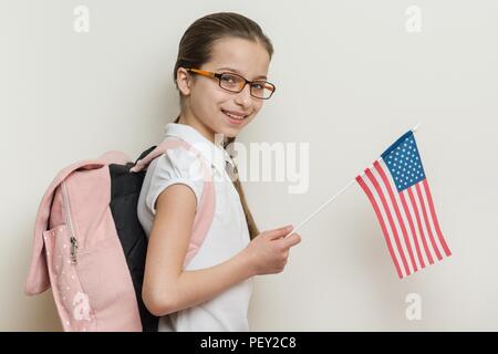 School child with a backpack holds the US flag, background bright wall in the school. Stock Photo