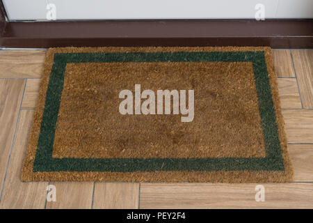 Brown natural rug with green contour in front of the white entrance door. Stock Photo