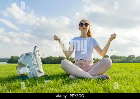 Young teenage girl practicing yoga on the grass in park, meditating Stock Photo