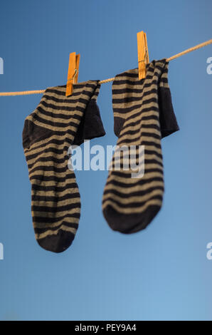 Pair of striped socks hanging on a clothesline against a blue sky background. Stock Photo