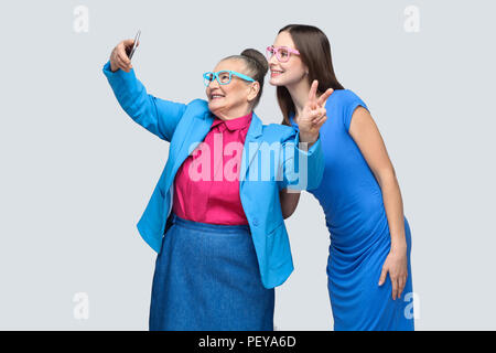 happy grandmother with granddaughter in blue dress and suit standing, posing and making selfie and toothy smiling. Relations in the family. indoor, st Stock Photo