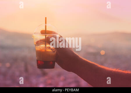Mans hand holding iced cofee against city streets in background Stock Photo