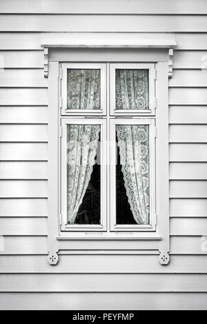 Exterior view of a window of a traditional wooden house in Norway, decorated with lace curtains. Stock Photo
