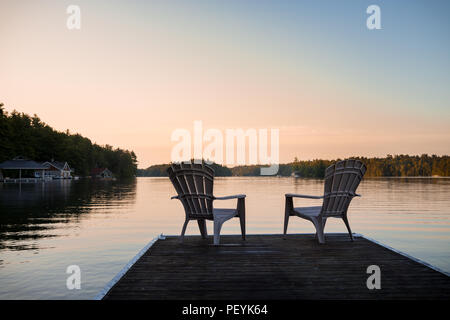 Muskoka chairs sitting at the end of a dock in front of Lake Joseph at sunrise. Stock Photo