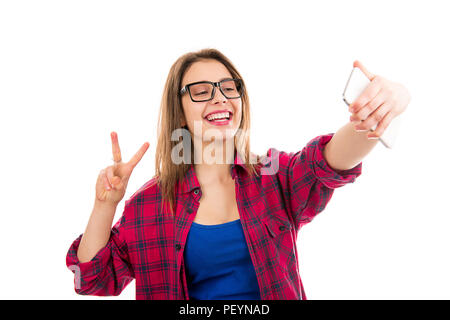 Charming young modern woman showing v-sign and taking selfie with smartphone isolated on white background Stock Photo