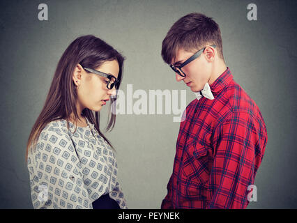 Side view of young man and woman looking down standing opposite with feelings of regret and sadness Stock Photo