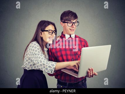 Young excited couple using laptop together and looking surprised with content standing on gray background Stock Photo