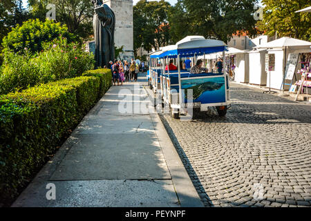 Tourists crowd around the statue of Gregory Nin as a cat scurries under a tourist tram outside the Golden Gate to Diocletian's Palace in Split Croatia Stock Photo