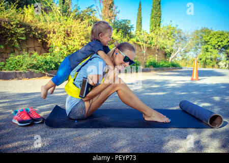 Sportive mother with child outdoors doing fitness excercise,  happy family together on workout, active healthy lifestyle Stock Photo