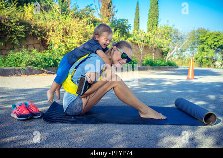 Sportive mother with child outdoors doing fitness excercise,  happy family together on workout, active healthy lifestyle Stock Photo